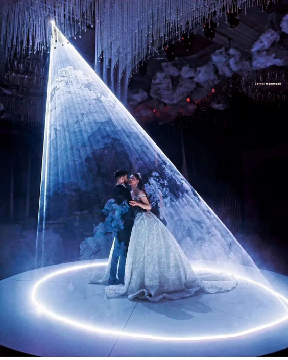 A couple in a spotlight on a stage with ethereal decorations, sharing a romantic moment.