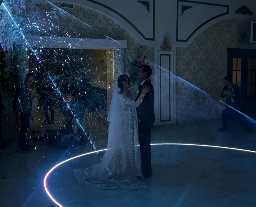 A couple in formal attire surrounded by a swirl of blue light on the dance floor.