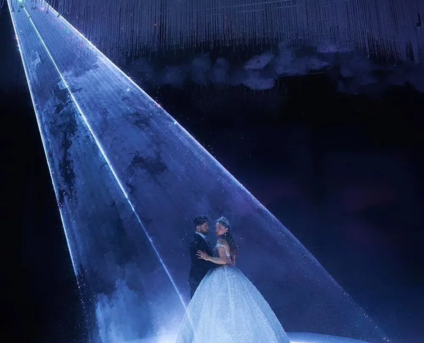 A couple in wedding attire under a bright spotlight in a dark room.