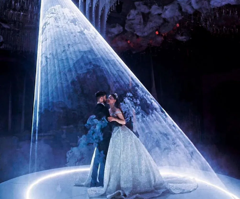 A couple in a spotlight on a stage with ethereal decorations, sharing a romantic moment.