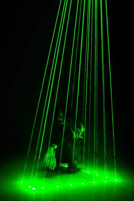 Figuras no escuro iluminadas por luzes laser verdes.