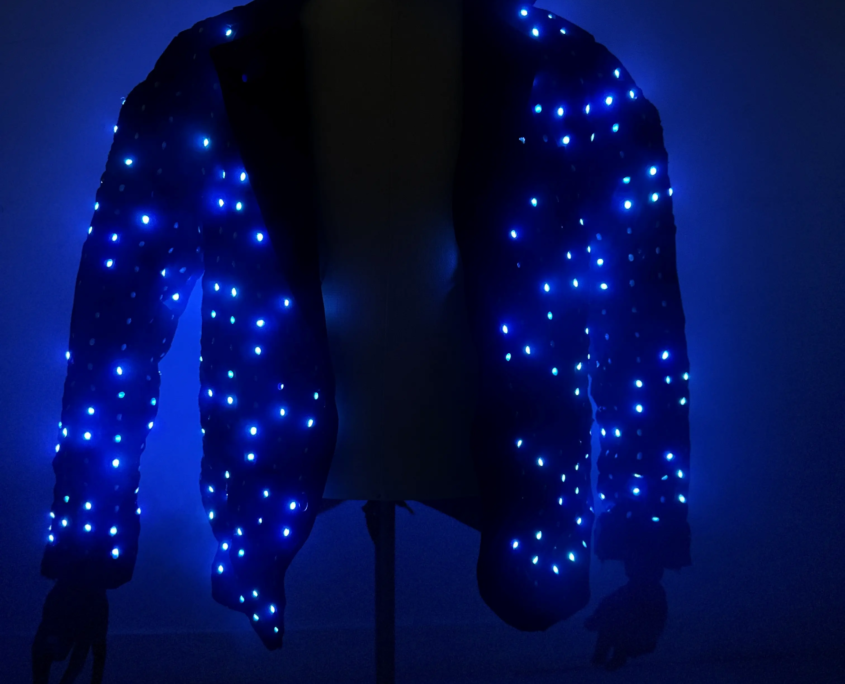 A jacket covered in blue LED lights, illuminated in a dark environment.