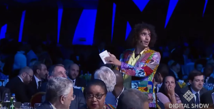 Um homem com terno colorido interage com o público durante um evento formal de tecnologia.